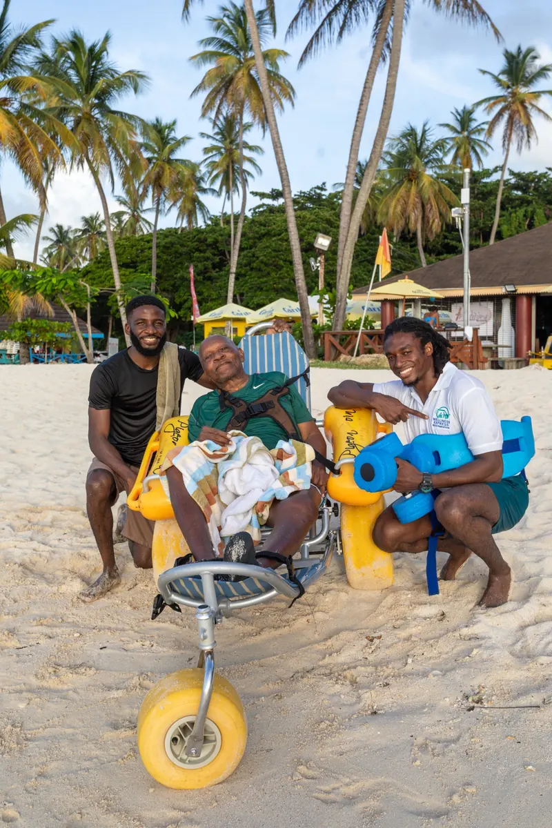 Client enjoying a Tobago beach in an all-terrain beach wheelchair with Wellness Express staff